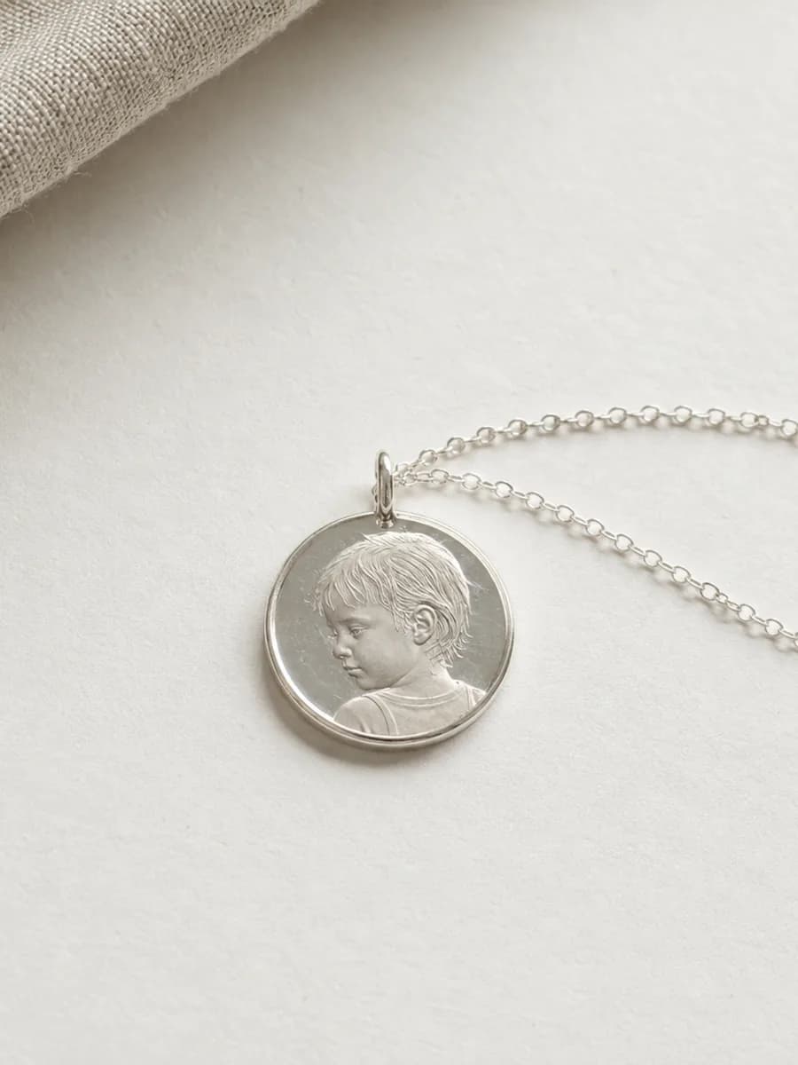 Silver pendant engraved with a child's portrait, on a fine chain beside folded linen