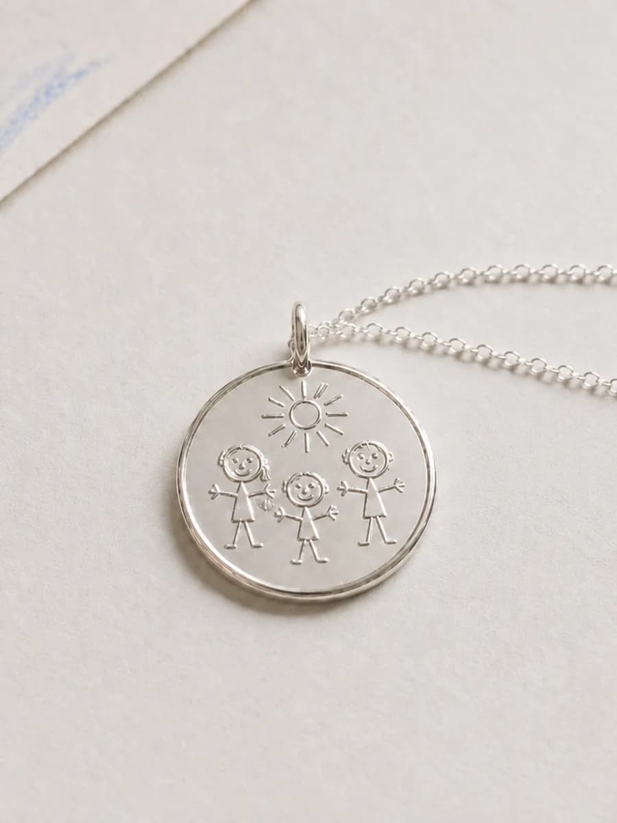 Silver pendant engraved with a child's drawing of a family under the sun